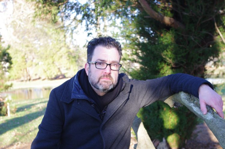 Een foto van Barry Kerckhoffs die met zijn linkerarm tegen een boom leunt op de achtergrond kun je bomen, gras en struiken zien