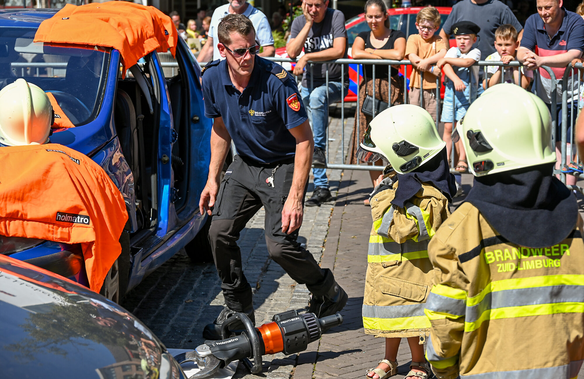 Een brandweerman met twee kinderen die een brandweerjas en -helm dragen tijdens de zwaailichtendag